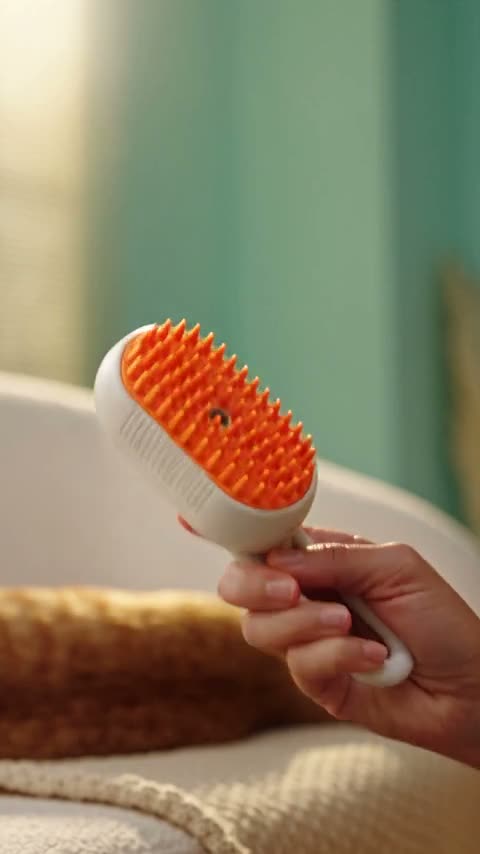 A hand draws an orange steam brush through a ginger cat’s fur on a cream sofa as steam rises from it, then the cat stretches out asleep while the brush sits on the side table.